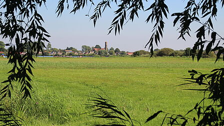 Een foto van een weiland en water met aan de horizon de bebouwing van de plaats Onderdijk