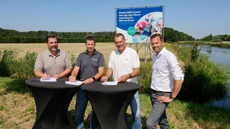 Bij het stuk land waar straks het zwembad wordt gebouwd, wordt de samenwerking bekrachtigd met een handtekening.