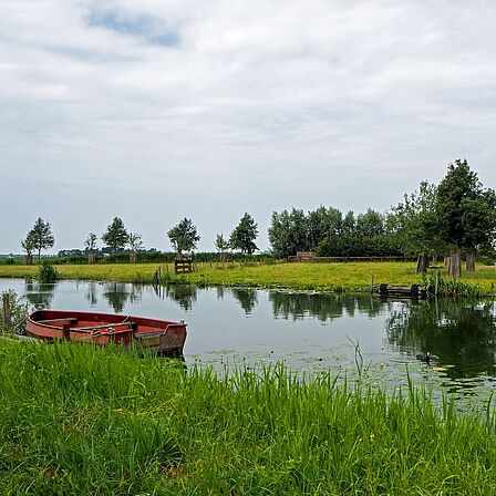 Afbeelding van het polderlandschap langs het Veldhuis met een bootje in het water. 